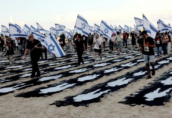 Des personnes portant des drapeaux israéliens traversent une installation commémorative sur la plage de Tel-Aviv pour marquer le troisième anniversaire de l'attaque du Hamas contre Israël, le 7 octobre 2026