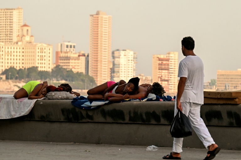 Un homme passe devant des femmes qui dorment sur le Malecon à La Havane lors d'une coupure de courant nationale, le 3 août 2026