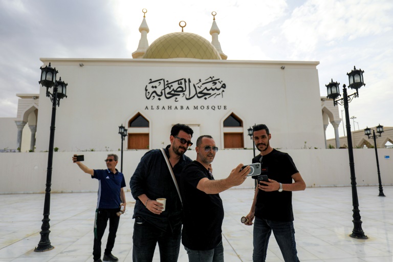Des passants posent pour un selfie devant la mosquée Sahaba, dans la ville de Derna, dans l'est de la Libye, le 15 mai 2026, après des efforts de reconstruction et de réurbanisation entrepris plus de deux ans après les pluies extrêmes provoquées par la tempête Daniel