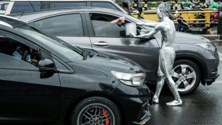 L'artiste de rue Ari Munandar (d), le corps recouvert de peinture argentée, fait la manche sous la pluie à un carrefour de Jakarta, le 1er avril 2025 en Indonésie