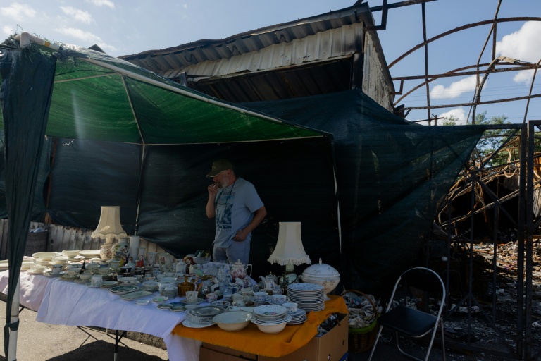 Vadym vend des objets sur son étal du marché aux puces de Potchaïna endommagé par une frappe russe, le 9 août 2026 à Kiev, en Ukraine