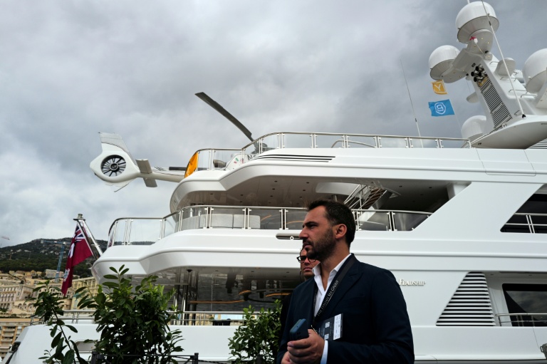 Un homme passe devant un superyacht amarré au port Hercule, avec un hélicoptère sur le pont, lors du Monaco Yacht Show, le 23 septembre 2026