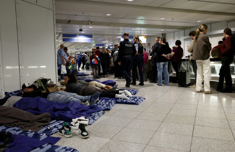 Des passagers dorment sur des matelas gonflables posés à même le sol tandis que d'autres font la queue à côté d'eux à l'aéroport international de Munich, dans le sud de l'Allemagne, tôt le matin du 4 octobre 2025