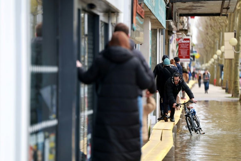 Des passants longent une rue inondée sur une passerelle de fortune, le 21 février 2026 à Saintes