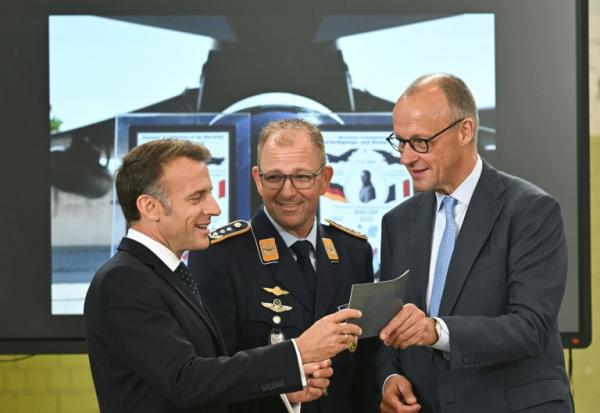Le chancelier allemand Friedrich Merz (D) et le président français Emmanuel Macron écoutent les explications d'un colonel à leur arrivée sur la base aérienne de Nörvenich, dans l’ouest de l'Allemagne, le 17 juillet 2026, où ils assisteront à une réunion du conseil de sécurité franco-allemand dans le cadre du conseil des ministres franco-allemand.