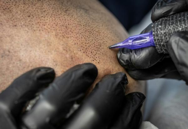 Remy, tatoueur professionnel, réalise une intervention de micropigmentation du cuir chevelu sur un client, dans son studio de Ginowan, à Okinawa au Japon, le 19 mai 2026