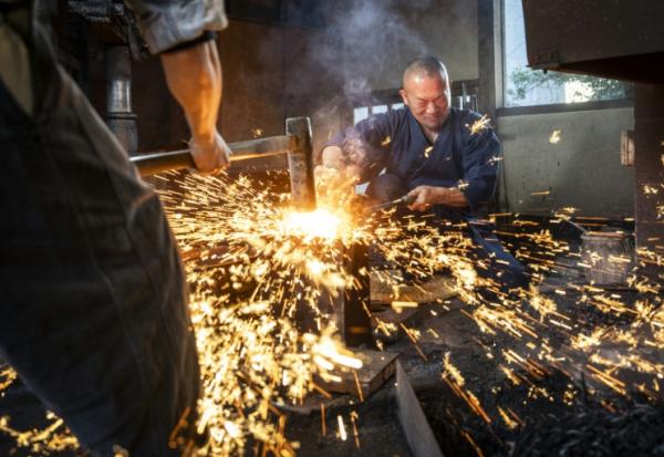 Le forgeron Akihira Kawasaki (d) maintient l'acier sur une enclume tandis que son apprenti Toru Watanabe martèle le métal pour forger des lames de katana, le 9 janvier 2026 à Misato, au Japon