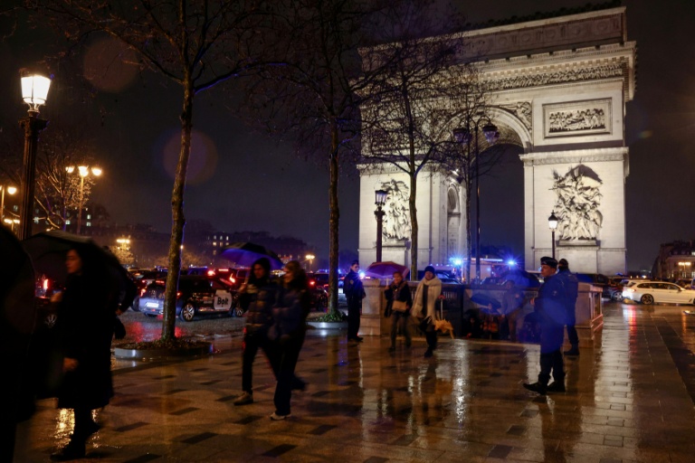 Des passants longent des policiers qui bloquent l'accès à un quartier de Paris le 13 février 2026, après qu'un homme armé d'un couteau a été blessé par la police sous l'Arc de Triomphe