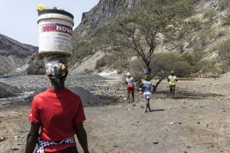 Des femmes portent des seaux en équilibre sur leur tête après avoir ramassé du sable noir destiné à la vente, près de Ribeira da Barca, le 20 mai 2026 au Cap-Vert