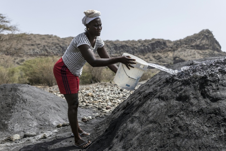 Vania Tavares verse de l'eau sur un tas de sable noir, sur une plage dégradée par l'exploitation commerciale, près de Ribeira da Barca, le 20 mai 2026 au Cap-Vert