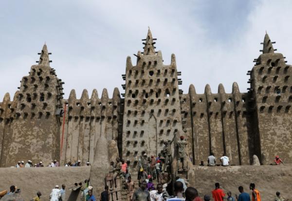 Des personnes utilisent du banco, un enduit de terre, pour le crépissage annuel de la grande mosquée de Djenné le 12 juin 2025