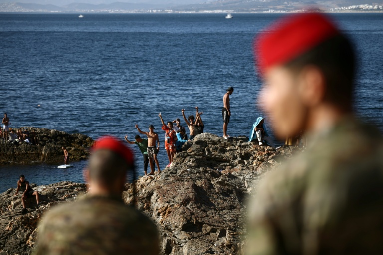 Des militaires espagnols regardent un groupe de jeunes gens sur des rochers à proximité du poste-frontière de l'enclave espagnole de Ceuta, le 2 août 2026 à Ceuta