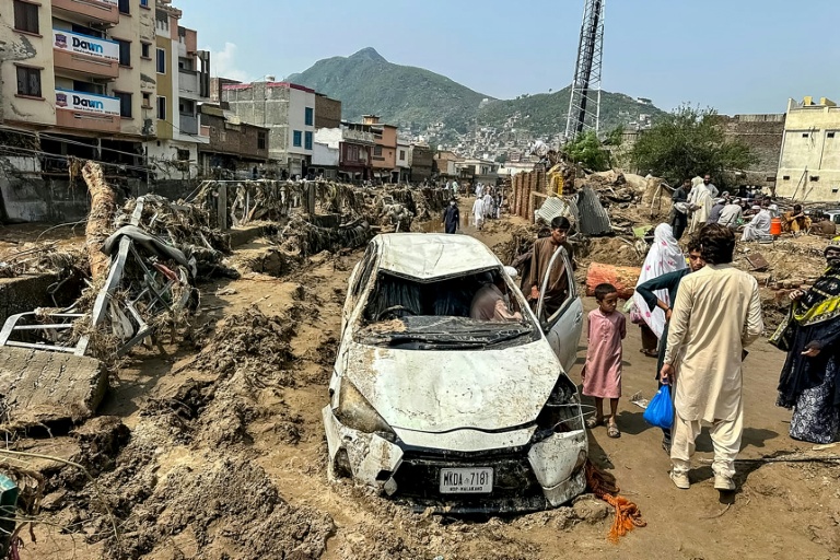 Des habitants de Mingora sont réunis autour d'un véhicule endommagé et de débris après l'effondrement de la route suite aux crues subites dans la province montagneuse de Khyber Pakhtunkhwa au Pakistan le 16 août 2025