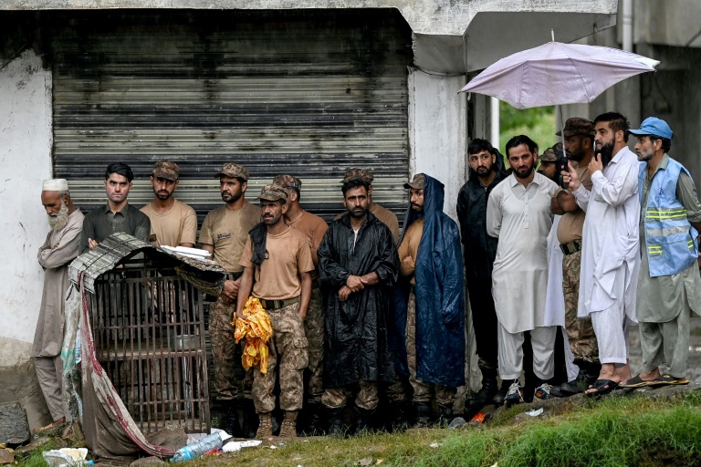Des sauveteurs et du personnel militaire s'abritent de la pluie sous le toit d'un bâtiment alors que le niveau des eaux de crue monte dans le district de Buner, dans la province  de Khyber Pakhtunkhwa, le 18 août 2025 au Pakistan