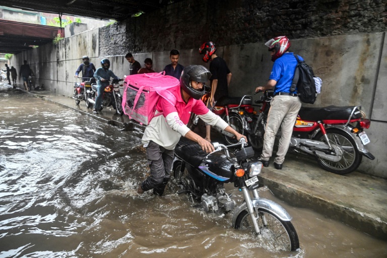 Abdullah Abbas (c), livreur de repas, pousse sa moto dans une rue inondée après de fortes pluies à Lahore, le 30 août 2025 au Pakistan