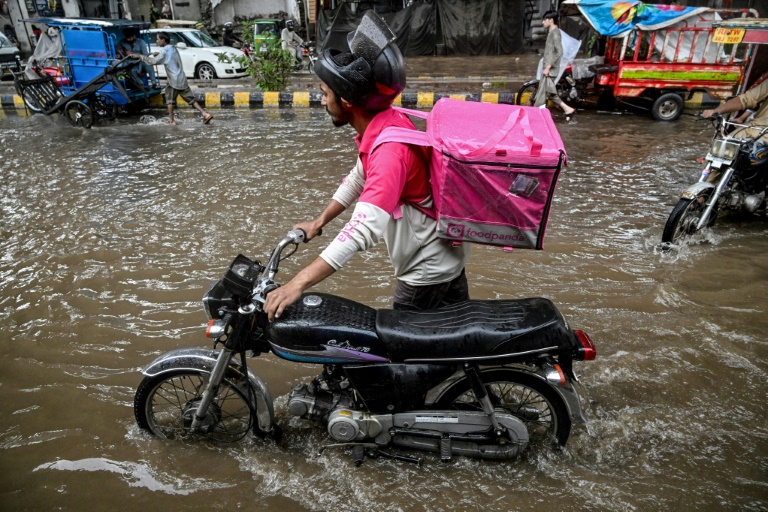 Abdullah Abbas, livreur de repas, pousse sa moto dans une rue inondée après de fortes pluies à Lahore, le 30 août 2025 au Pakistan