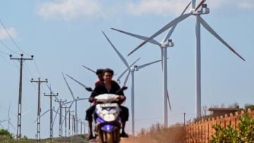 Cette photo, prise le 2 octobre 2026, montre un motard passant devant des éoliennes installées le long d'une route de la péninsule de Mannar, au Sri Lanka