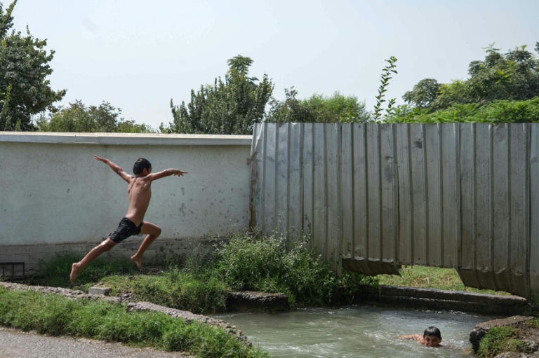 Des enfants sautent dans un canal d'irrigation qui traverse le village de Kolkhozobod, dans le sud-ouest du Tadjikistan, le 27 août 2025