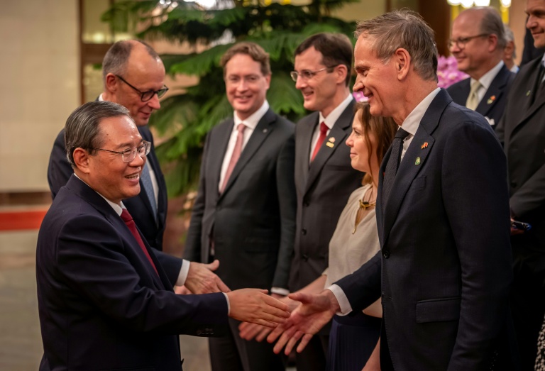 Le premier ministre chinois Li Qiang (g) serre la main du patron de Volkswagen Oliver Blume (d), le 25 février 2026 à Pékin, lors de la visite du chancelier allemand Friedrich Merz en Chine