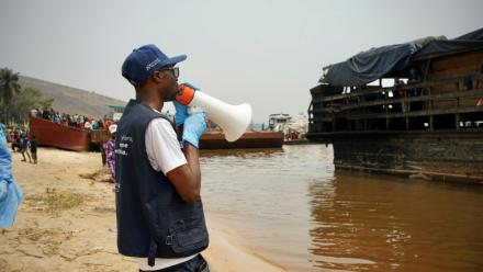 Mégaphone à la main, Yves Matwa, agent de la riposte à Ebola, passe les consignes aux passagers d’une baleinière, au port de Bende-Bende, commune de Maluku, à 70 km au nord-est de Kinshasa, le 20 août 2026