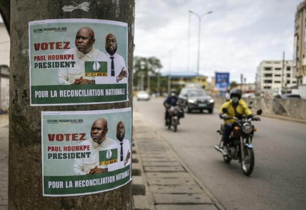 Des habitants de la capitale béninoise circulent à moto et en voiture près d'une affiche électorale, le 9 avril 2026 à Cotonou