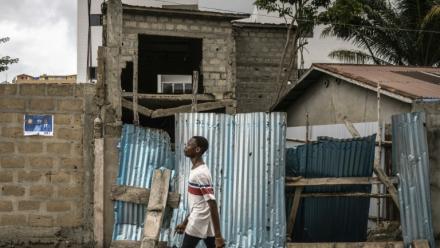 Un jeune homme marche dans un quartier de Cotonou le 9 avril 2026, près d'une affiche électorale placardée au mur 