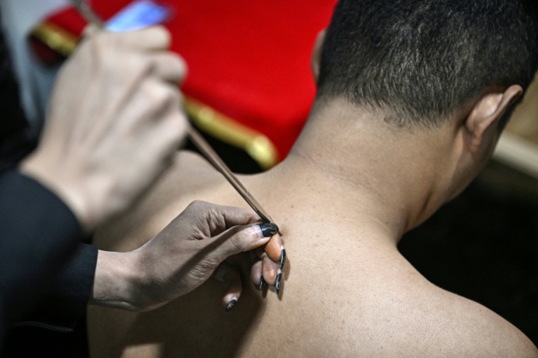 L'astrologue birman en exil Linn Nhyo Taryar marque d'un tatouage le dos d'un client, le 7 décembre 2025 à Bangkok 