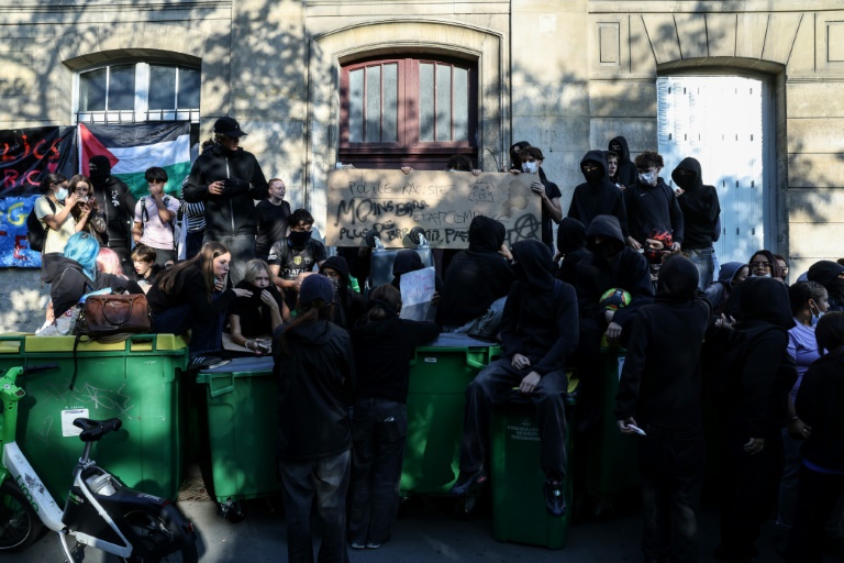 Des manifestants se tiennent debout sur des poubelles empilées à l'entrée du lycée Arago à Paris, le 29 septembre 2026