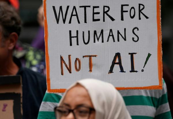 Une personne brandit une pancarte indiquant "De l'eau pour les humains, pas pour l'IA" lors d'une manifestation contre l'approbation d'un centre de données prévu dans les plans de réaménagement du quartier de Brick Lane, le 4 septembre 2026 à Londres