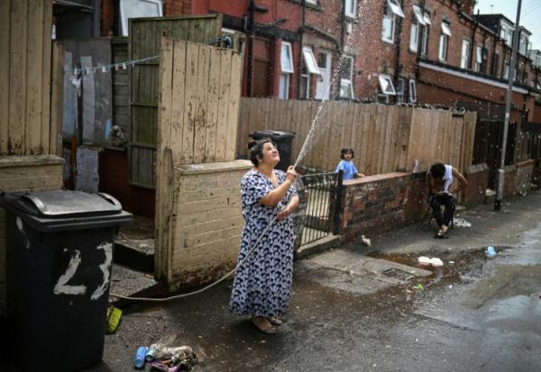 Une femme asperge une allée devant chez elle pour rafraichir à Leeds en Angleterre le 25 juin 2026