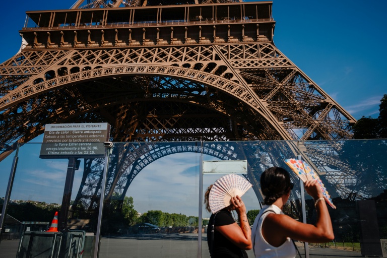 Des touristes se protègent du soleil avec des éventails en passant devant la tour Eiffel, fermée plus tôt en raison de la canicule, le 11 juillet 2026 à Paris