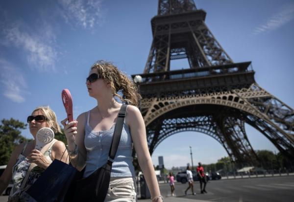 Deux femmes se rafraîchissent à l'aide de ventilateurs portables, au pied de la tour Eiffel, à Paris, le 10 juillet 2026