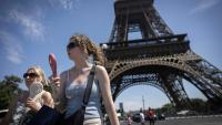 Deux femmes se rafraîchissent à l'aide de ventilateurs portables, au pied de la tour Eiffel, à Paris, le 10 juillet 2026