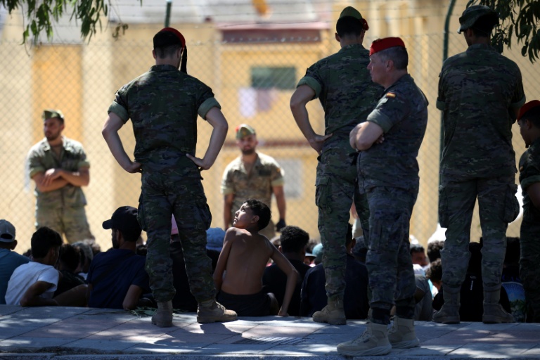 Un jeune migrant regarde un militaire espagnol, avant d'être escorté avec d'autres migrants vers le Maroc, le 2 août 2026 dans l'enclave espagnole de Ceuta