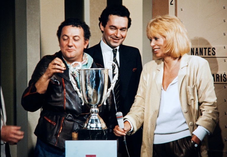 L'humoriste Coluche, à gauche, et l'actrice Mireille Darc, à droite, procèdent au tirage au sort des quarts de finale de la coupe de France, le 17 avril 1983, durant l'émission Télé foot animée par Michel Denisot, au centre