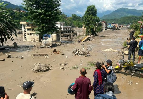 Des habitants observent des maisons partiellement submergées dans des eaux boueuses à la suite d'inondations soudaines survenues à Trishuli Bazar, dans le district de Nuwakot au Népal, le 26 août 2026.