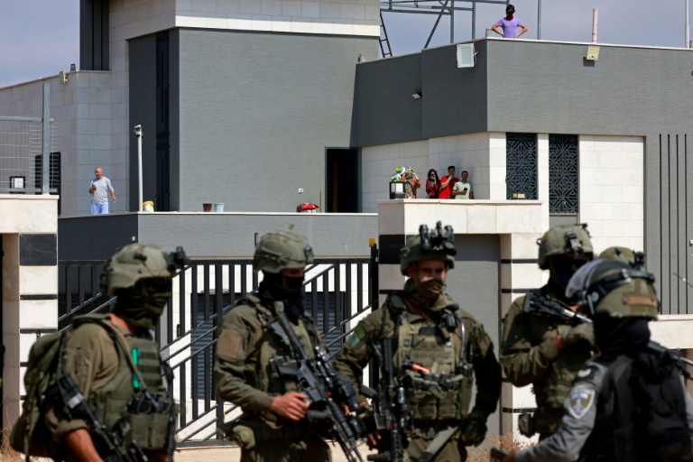 Des soldats israéliens devant l'entrée d'une maison palestinienne assiégée par des colons israéliens dans le village de Qusra, au sud de Naplouse, alors que des militants de gauche israéliens déposent des vivres pour ses habitants, le 14 août 2026 en Cisjordanie occupée