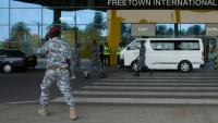 Des agents de sécurité escortent des migrants vers un centre de l'Agence nationale de santé publique (NPHA) après leur arrivée à l'aéroport international de Freetown, le 20 mai 2026 à Lungi, en Sierra Leone