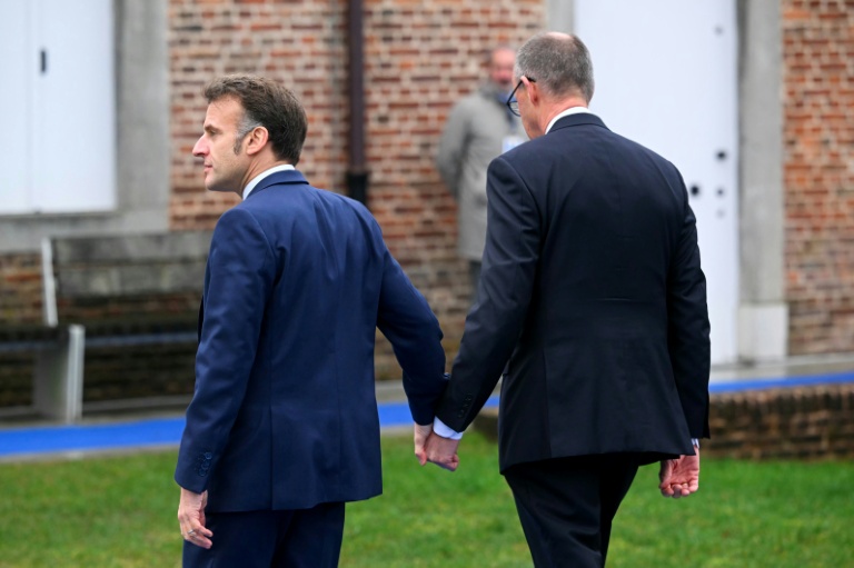 Emmanuel Macron (G) et Friedrich Merz se tiennent la main à leur arrivée au sommet informel de l'UE au château belge d'Alden Biesen en Belgique le 12 février 2026