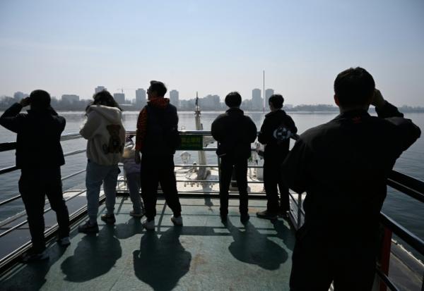 Des touristes observent la ville nord-coréenne de Sinuiju (arrière-plan) depuis un bateau touristique sur le fleuve Yalu, dans la ville frontalière de Dandong, dans le nord-est de la Chine, le 26 mars 2026