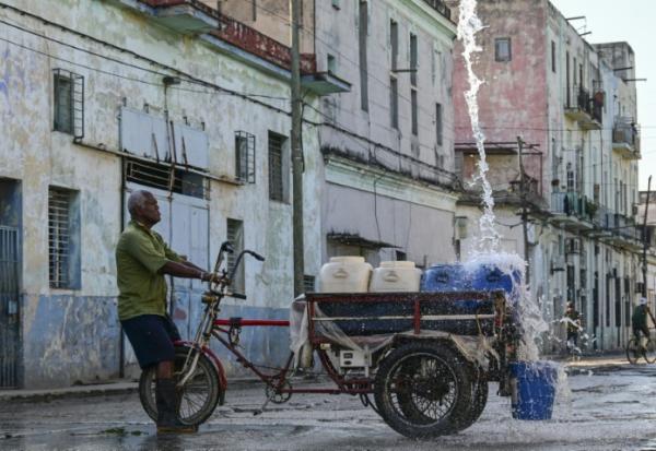Un homme remplit des récipients d'eau à un point de ravitaillement public dans une rue de La Havane, le 5 octobre 2026