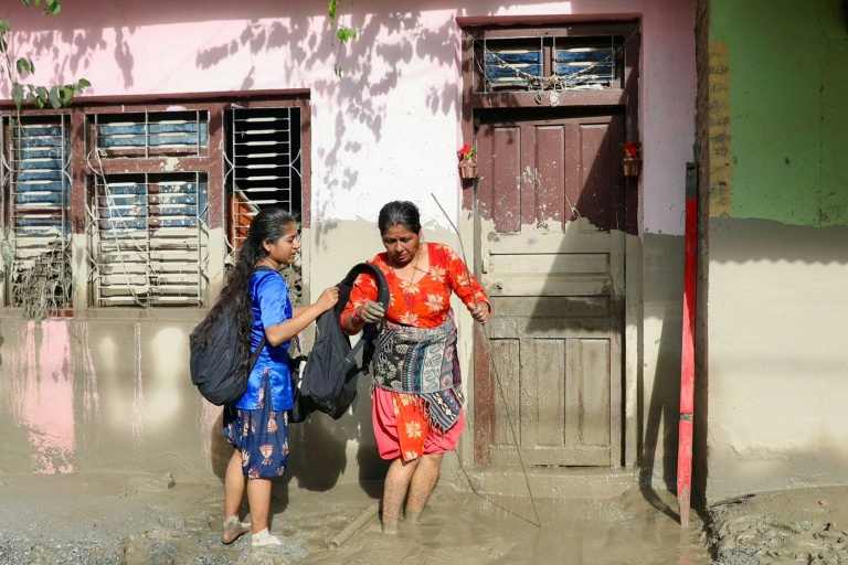 Des femmes devant une maison portant des traces de boue indiquent le niveau de l’eau après des crues dévastatrices près de Devighat, au Népal, le 27 août 2026