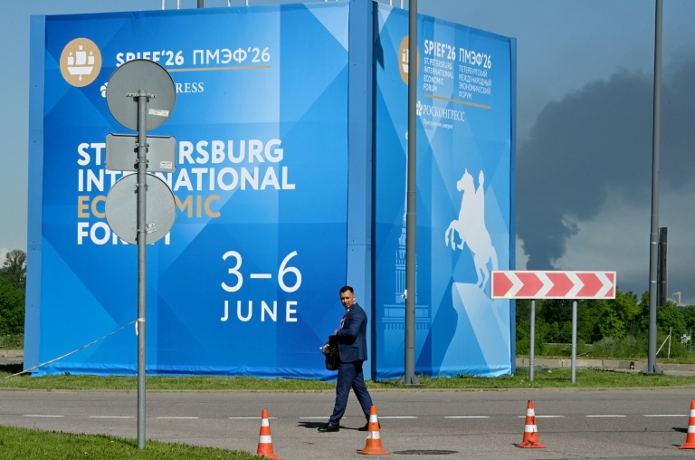 Un homme passe devant des affiches du Forum économique international de Saint-Pétersbourg alors que de  la fumée s'élève en arrière-plan après des frappes de drones ukrainiens, le 3 juin 2026