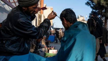 Un barbier coupe les cheveux d'un client dans une rue de Kaboul le 11 février 2026