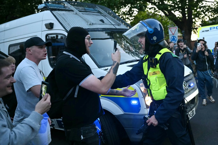 Des manifestants font face à un policier lors d'un rassemblement dans le centre d'Epping, au nord-est de Londres, le 20 juillet 2025