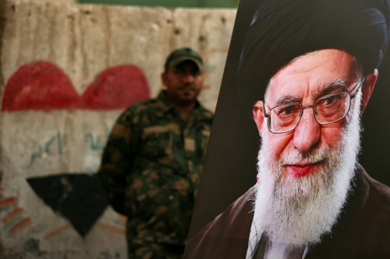 Un membre des Forces de mobilisation populaire irakiennes se tient derrière un portrait du guide suprême iranien défunt Ali Khamenei, à la veille de son cortège funère, au mausolée de l'imam Hussein à Karbala, en Irak, le 7 juillet 2026