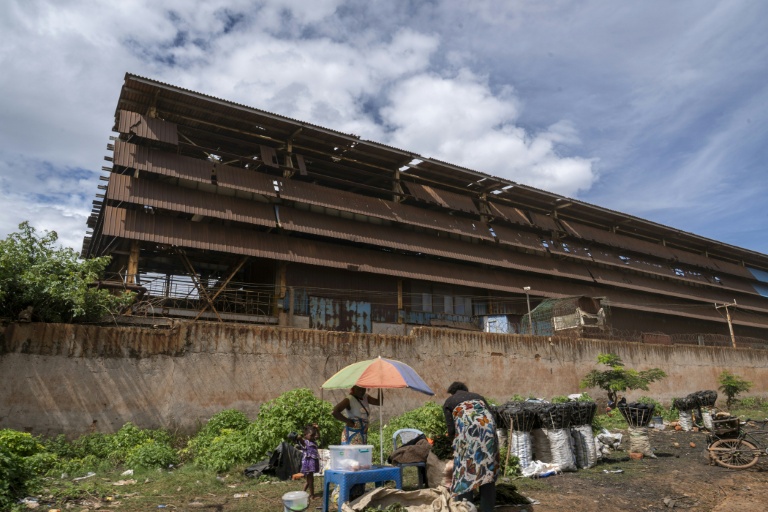 Une femme vend de la nourriture et du charbon devant les murs de l'usine minière chinoise Congo Dongfang Mining (CDM) à Lubumbashi en République démocratique du Congo le 24 novembre 2025