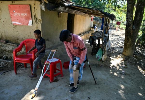 Ali Hossain (à droite), un Bangladais de 40 ans qui a perdu une jambe à cause d’une mine lorsqu'il ramassait du bois, retire sa prothèse devant sa maison dans le district de Bandarban le 19 décembre 2025