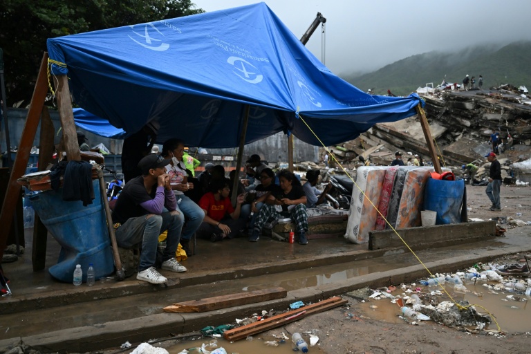 Des rescapés du double séisme s’abritent sous une bâche tandis que les secouristes fouillent les décombres des immeubles effondrés à Caraballeda, dans l’État de La Guaira, au Venezuela, le 11 juillet 2026