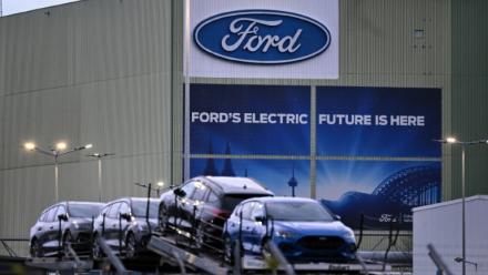 Des voitures du constructeur automobile américain Ford sont alignées sur un camion transporteur devant le logo de l'entreprise à l'usine Ford de Cologne, dans l'ouest de l'Allemagne, le 25 novembre 2024